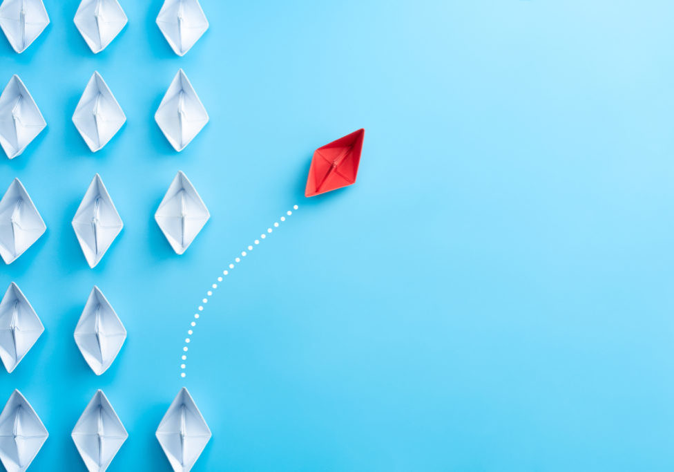 Group of white paper ship in one direction and one red paper ship pointing in different way on blue background. Business for innovative solution concept.